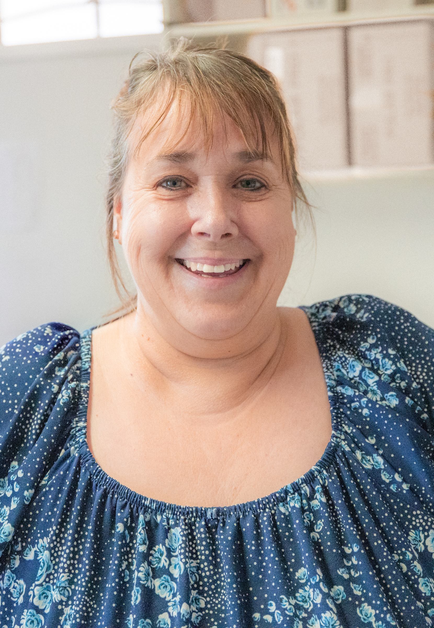 Portrait of a smiling woman with short blonde hair and a blue floral top indoors.