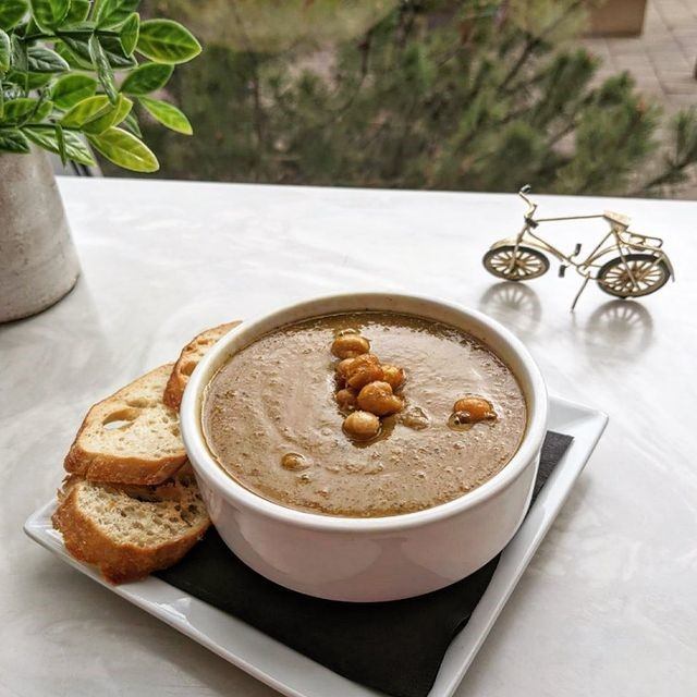 Soup with bread slices, served near a window with a bicycle decor.