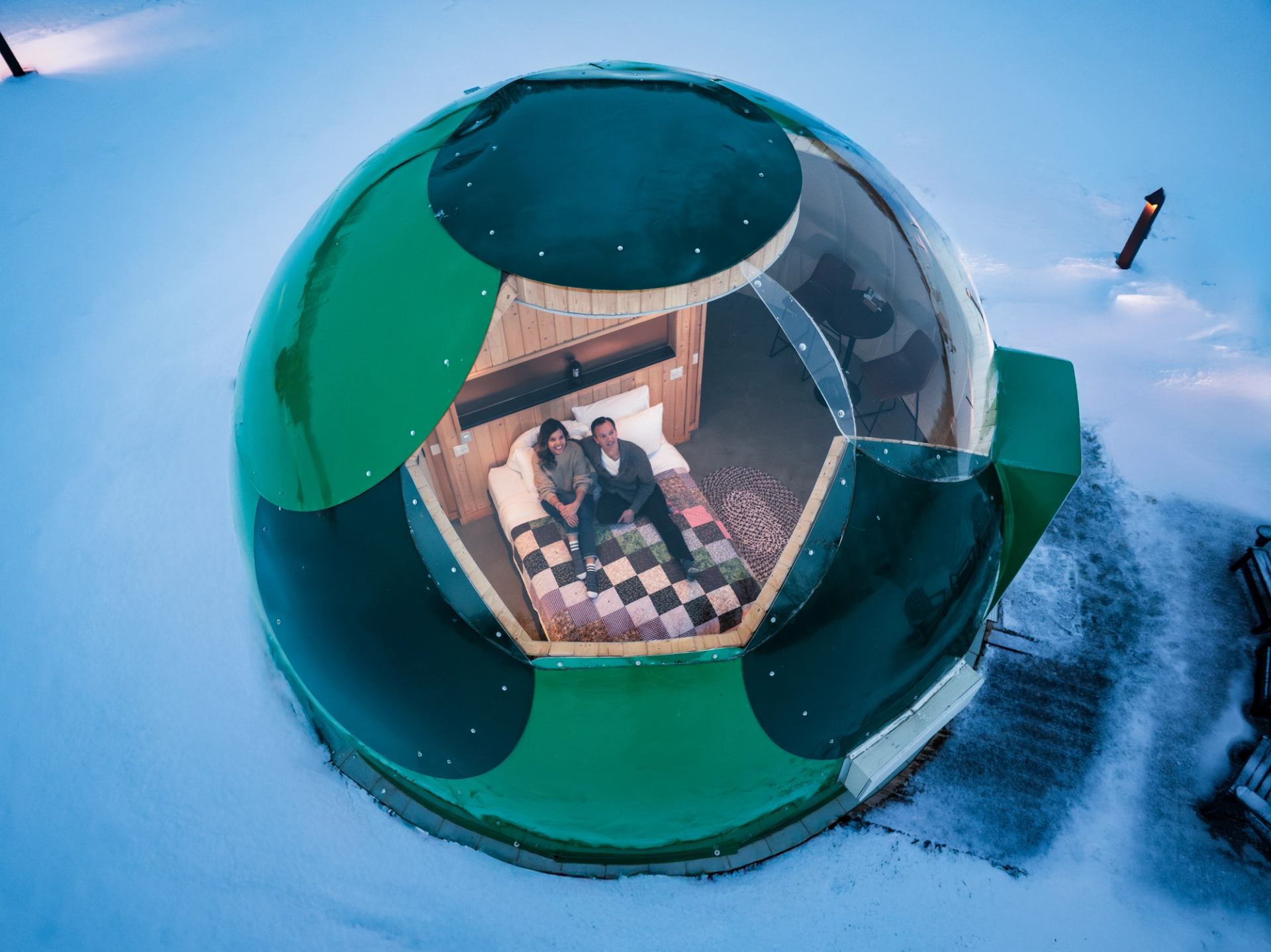Transparent dome with bed and quilt in snowy setting at Métis Crossing Sky Watching Domes.