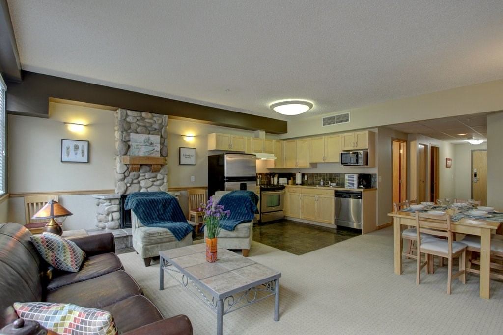 Open-concept living area with stone fireplace, modern kitchen, and dining table.