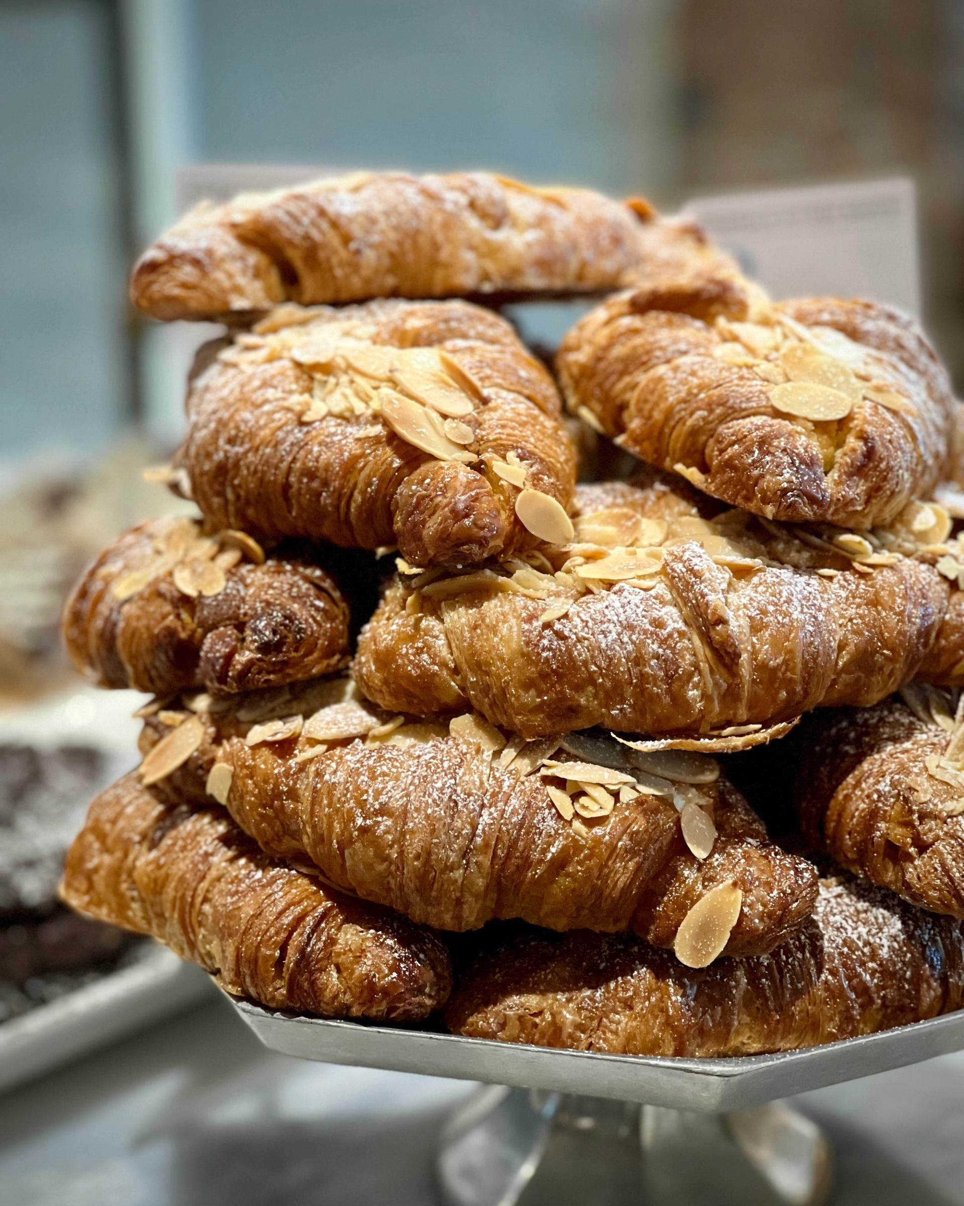 Almond croissants stacked on a display stand, dusted with powdered sugar.