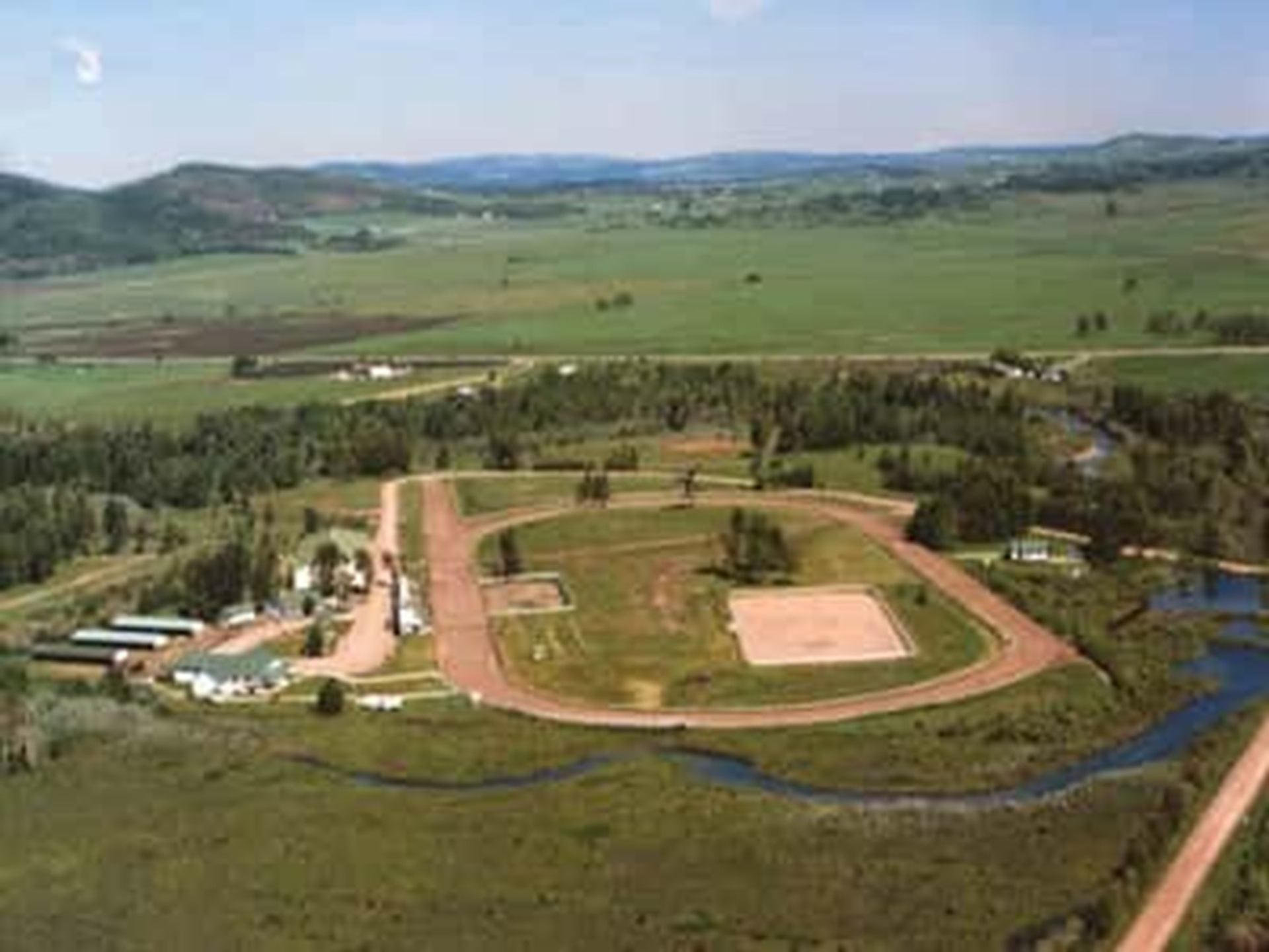 Aerial view of rural racetrack complex surrounded by fields, trees and winding river.