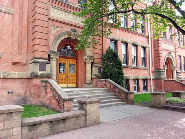 Historic red-brick building with arched entrance and greenery at Edmonton Public Schools Museum.