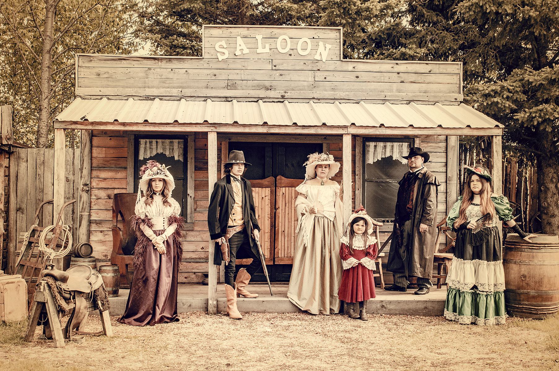 People in Western costumes pose on porch beneath SALOON sign.