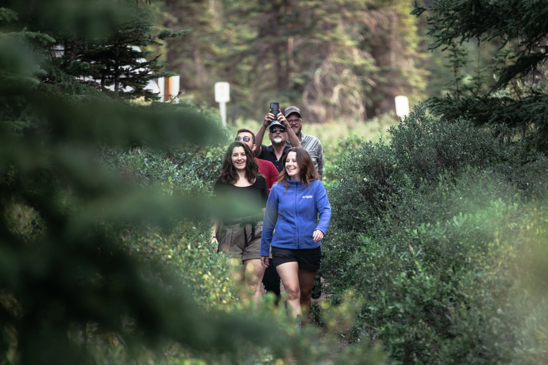 Group of people walking along a narrow forest trail surrounded by dense greenery.