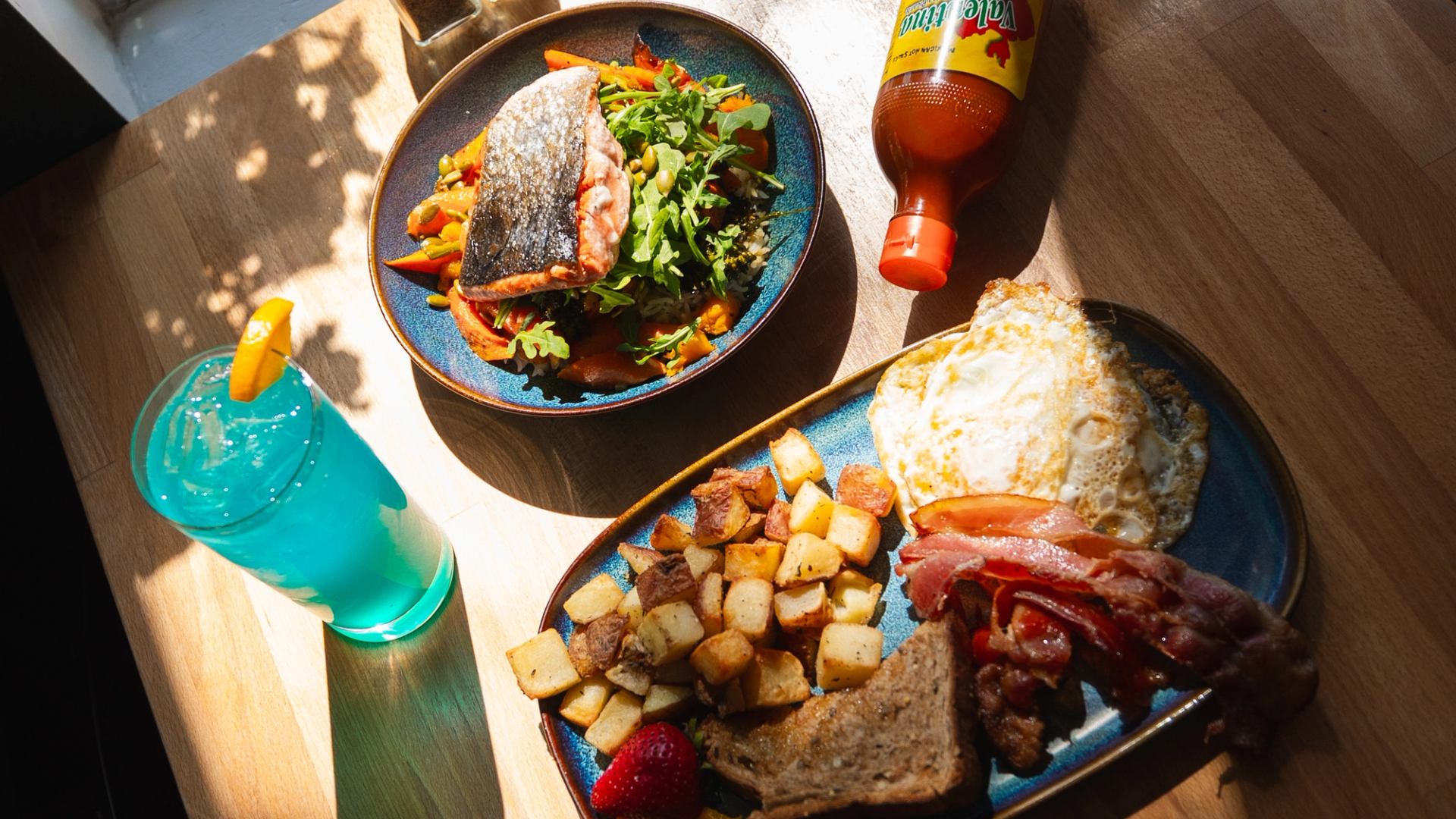 Table with salmon salad, breakfast plate, and a bright blue drink.