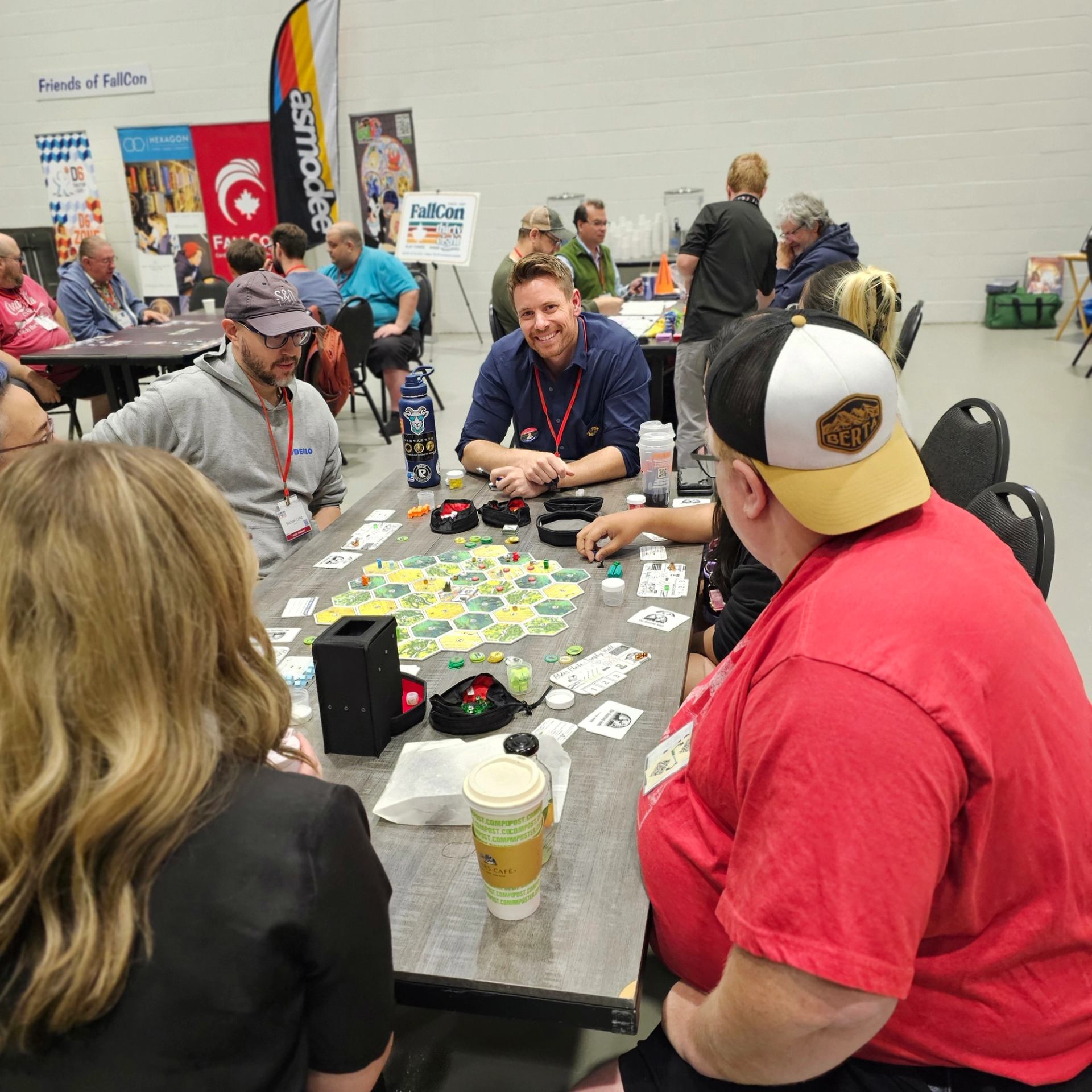 Board game players sit around a table at FallCon convention, focused on hex tiles.