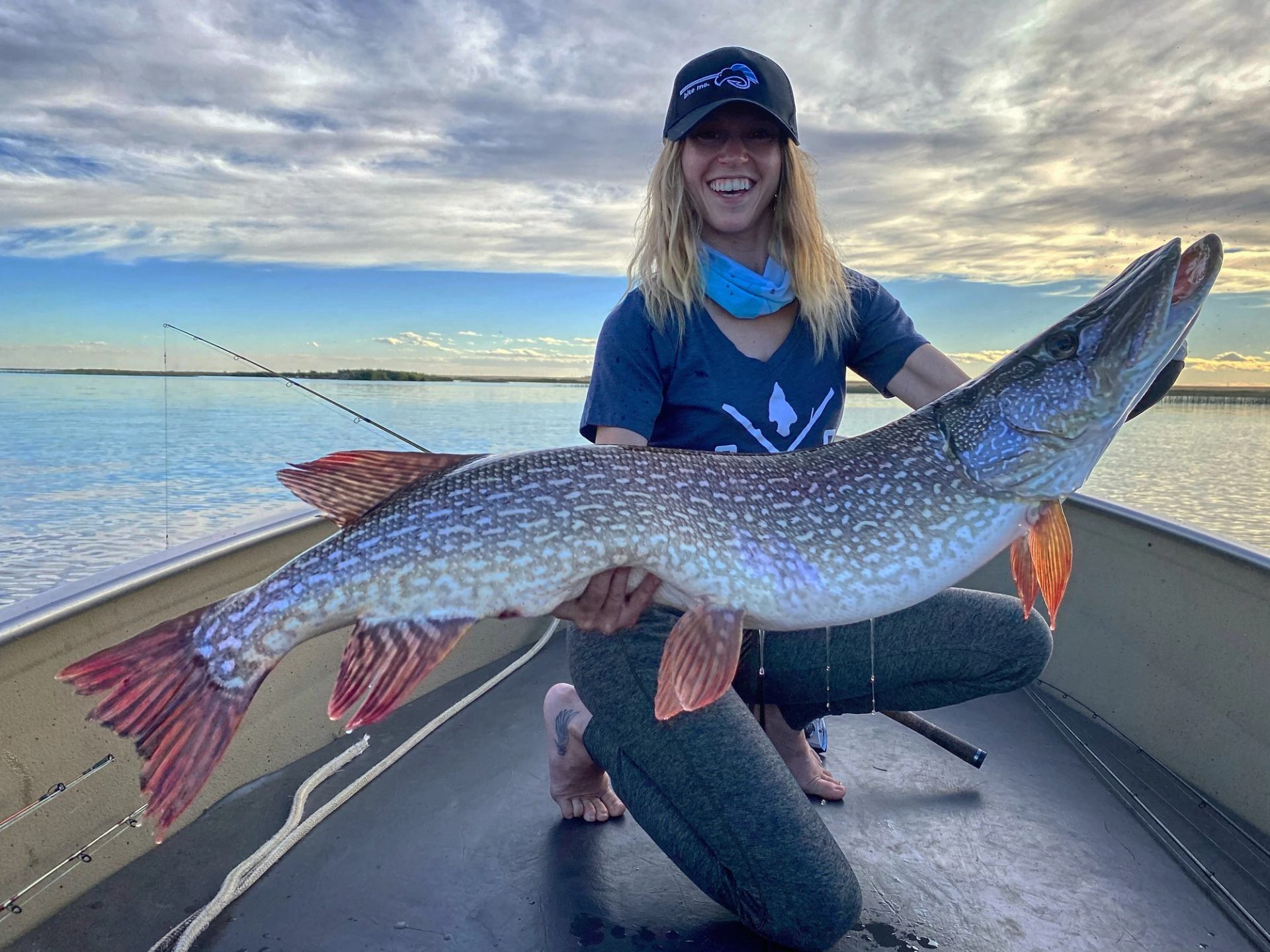 Large fish held on a boat with calm water and a colorful sunset sky in the background.