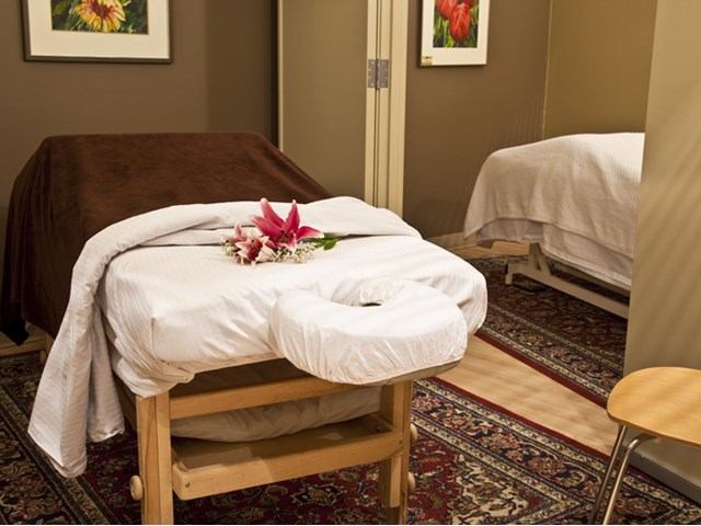 Spa treatment room with massage table, folded linens, and flowers on white cover.
