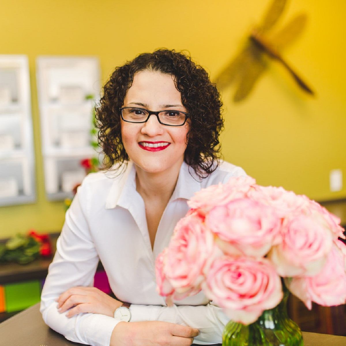 Pink rose bouquet on table with person seated and dragonfly decor behind.