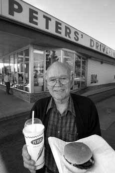 Gus Pieters, founder of the restaurant, holds a burger and milkshake while standing outside the drive-in restaurant.