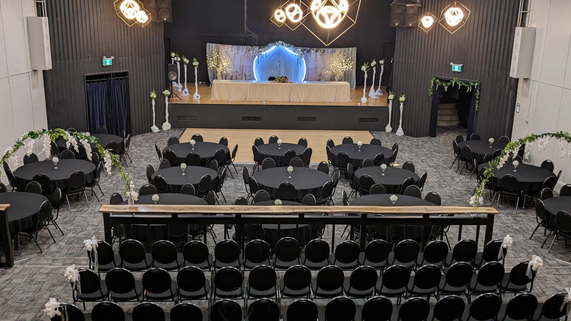 Banquet hall with round tables, floral arches and decorated stage with glowing backdrop.