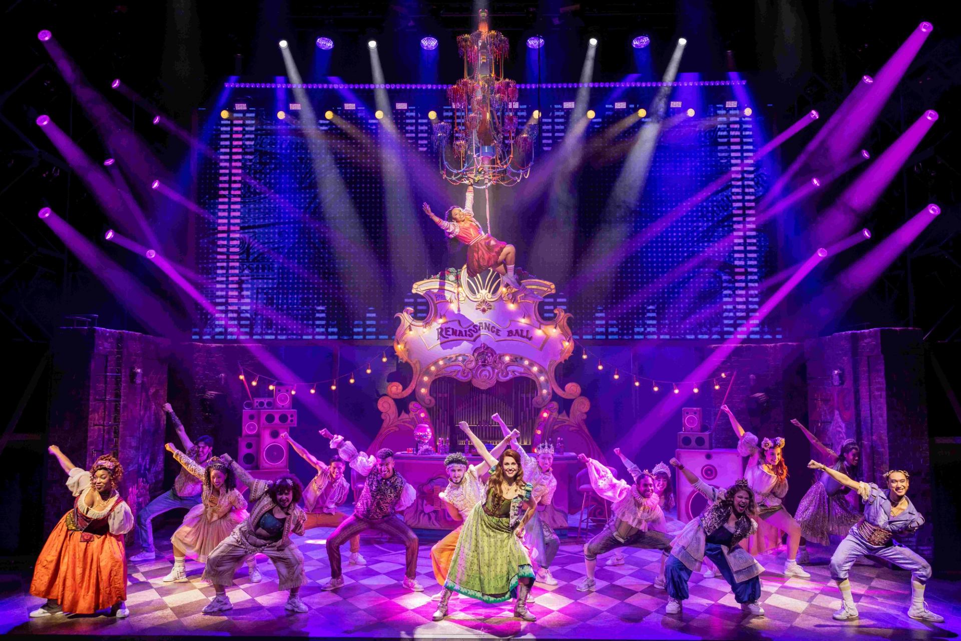 Stage musical cast dances under purple lights before Renaissance Ball sign and chandelier..