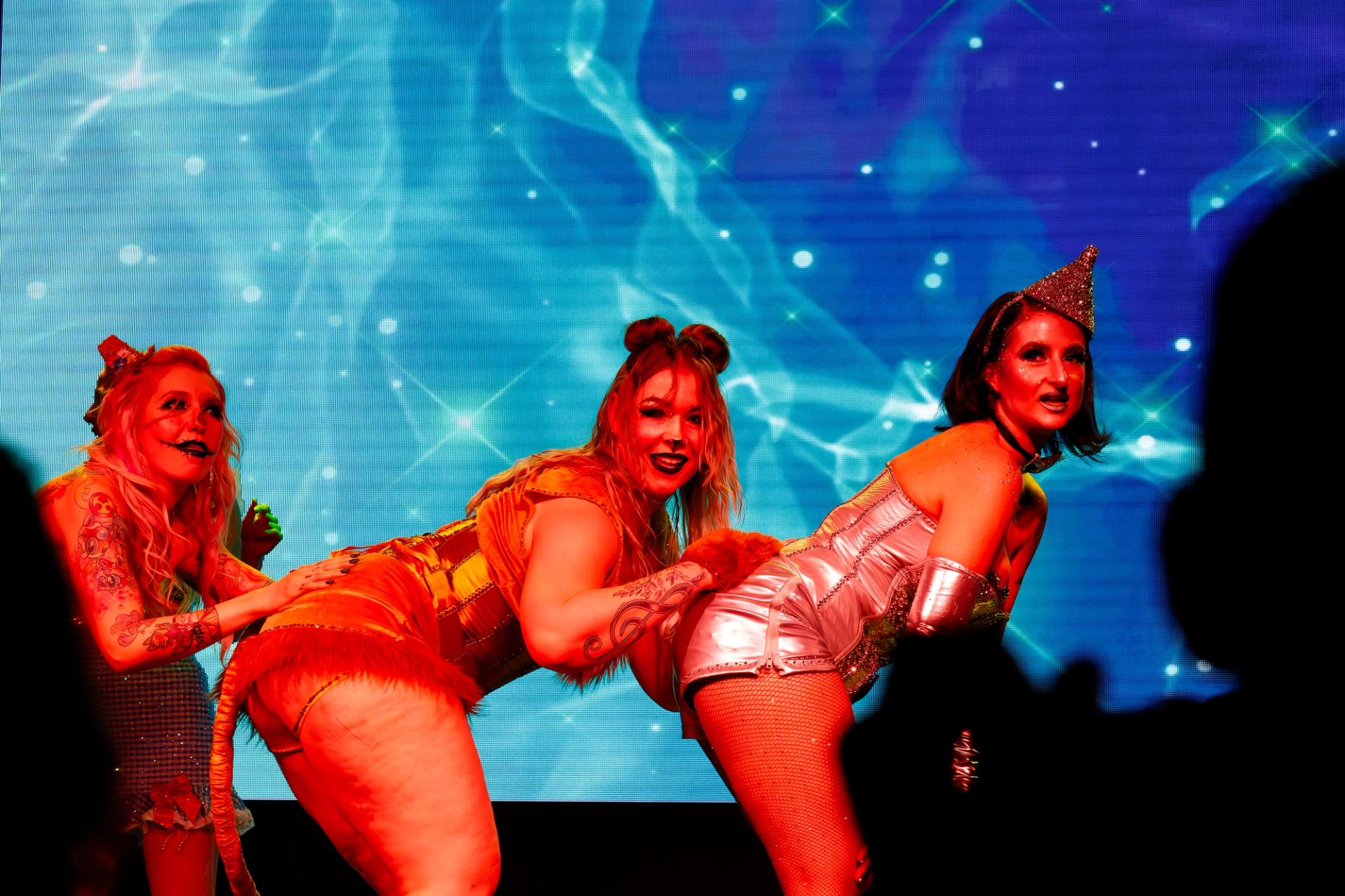 Three costumed performers on stage with starry blue backdrop in dynamic pose.