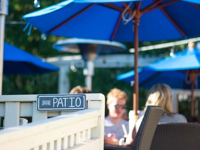 Patio sign on white railing with blue umbrellas and diners in background.