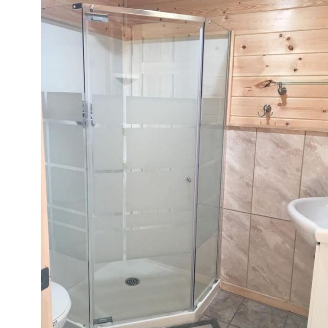 Glass shower enclosure in a rustic bathroom with wood paneling and tiled walls.