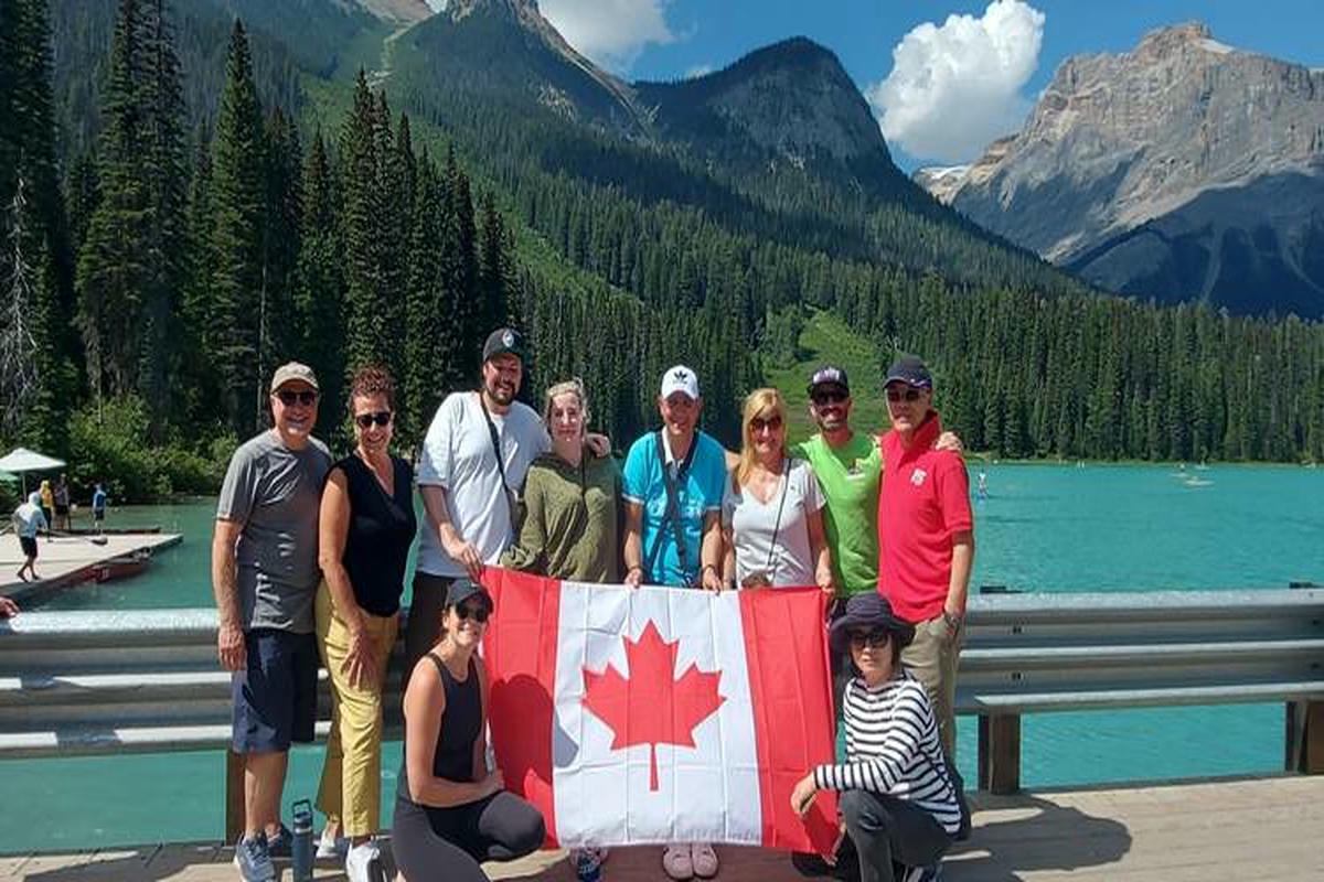 Group of people holding a Canadian flag beside turquoise lake and forested mountains.