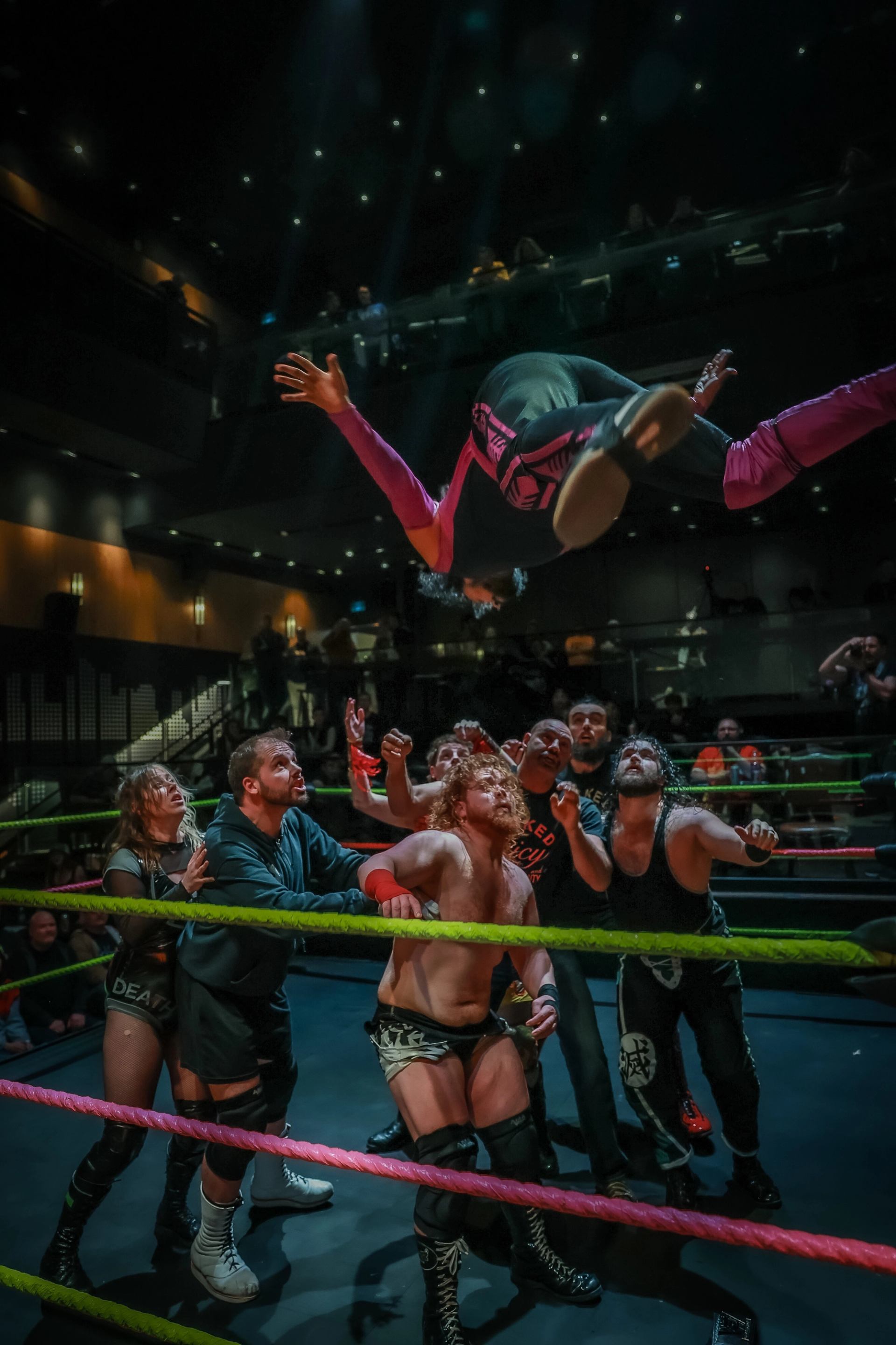 Wrestler leaps from above onto a group waiting in the ring during a match.