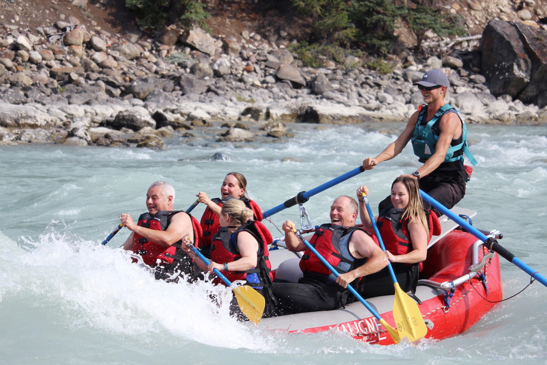 Group paddling hard through splashing whitewater in a red raft on a fast-moving river.