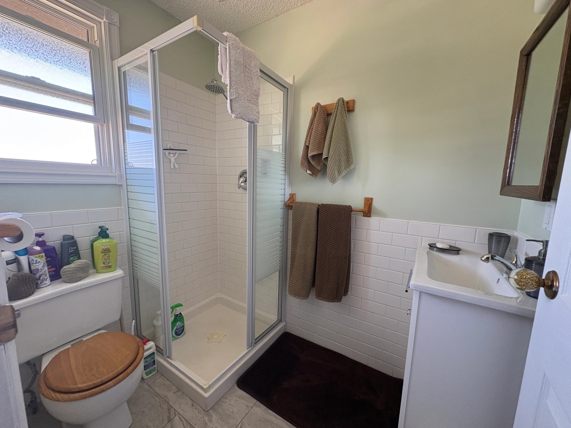 Small bathroom with corner shower, toilet, sink, towels and assorted toiletries.