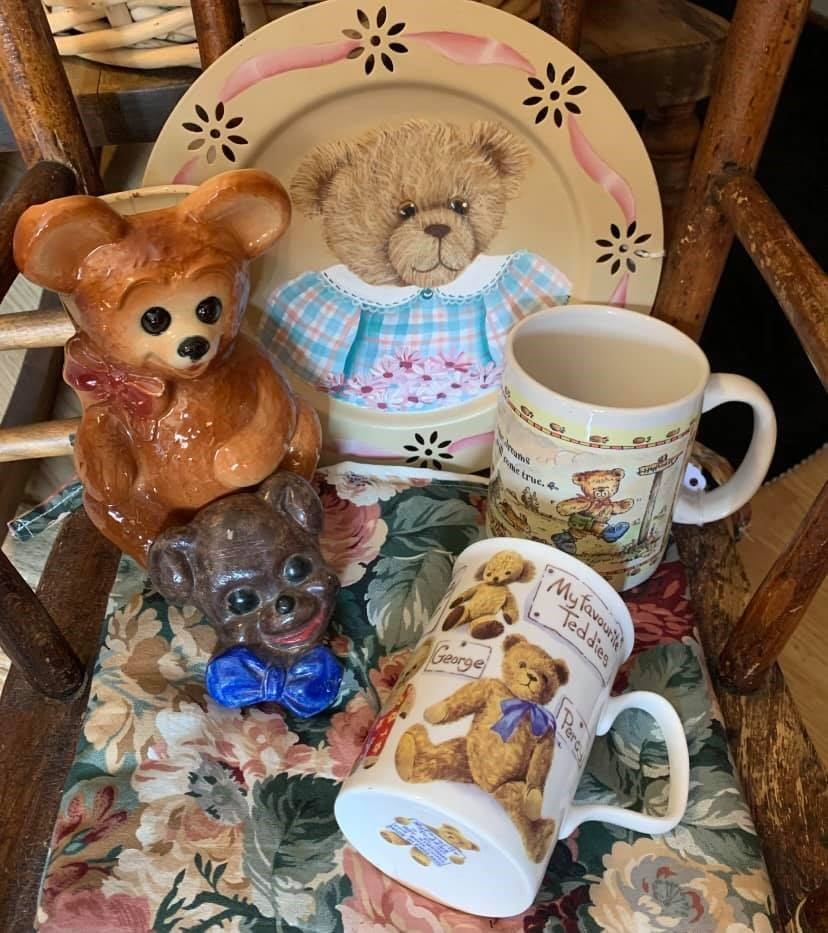 Teddy bear–themed mugs, figurines, and a painted plate arranged on a floral chair.