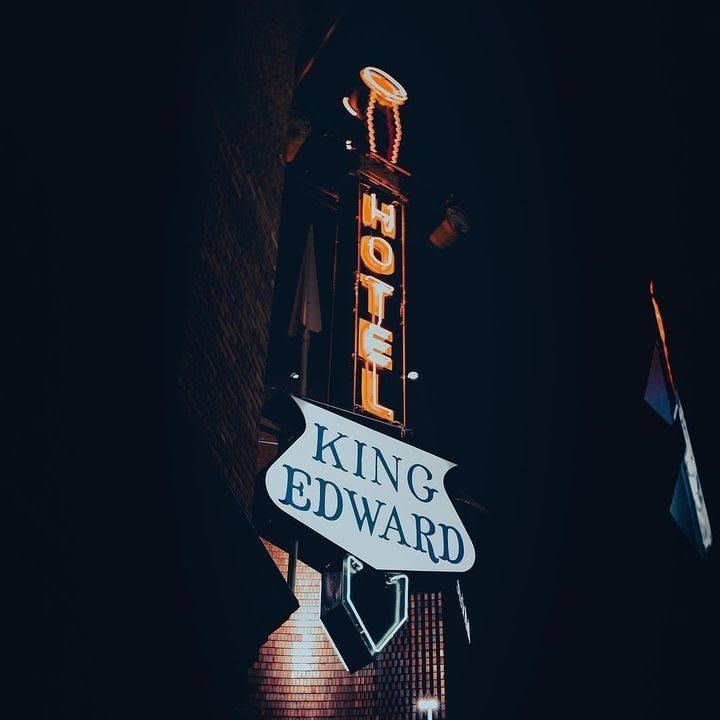 Neon hotel sign reading King Edward glows against a dark night sky.