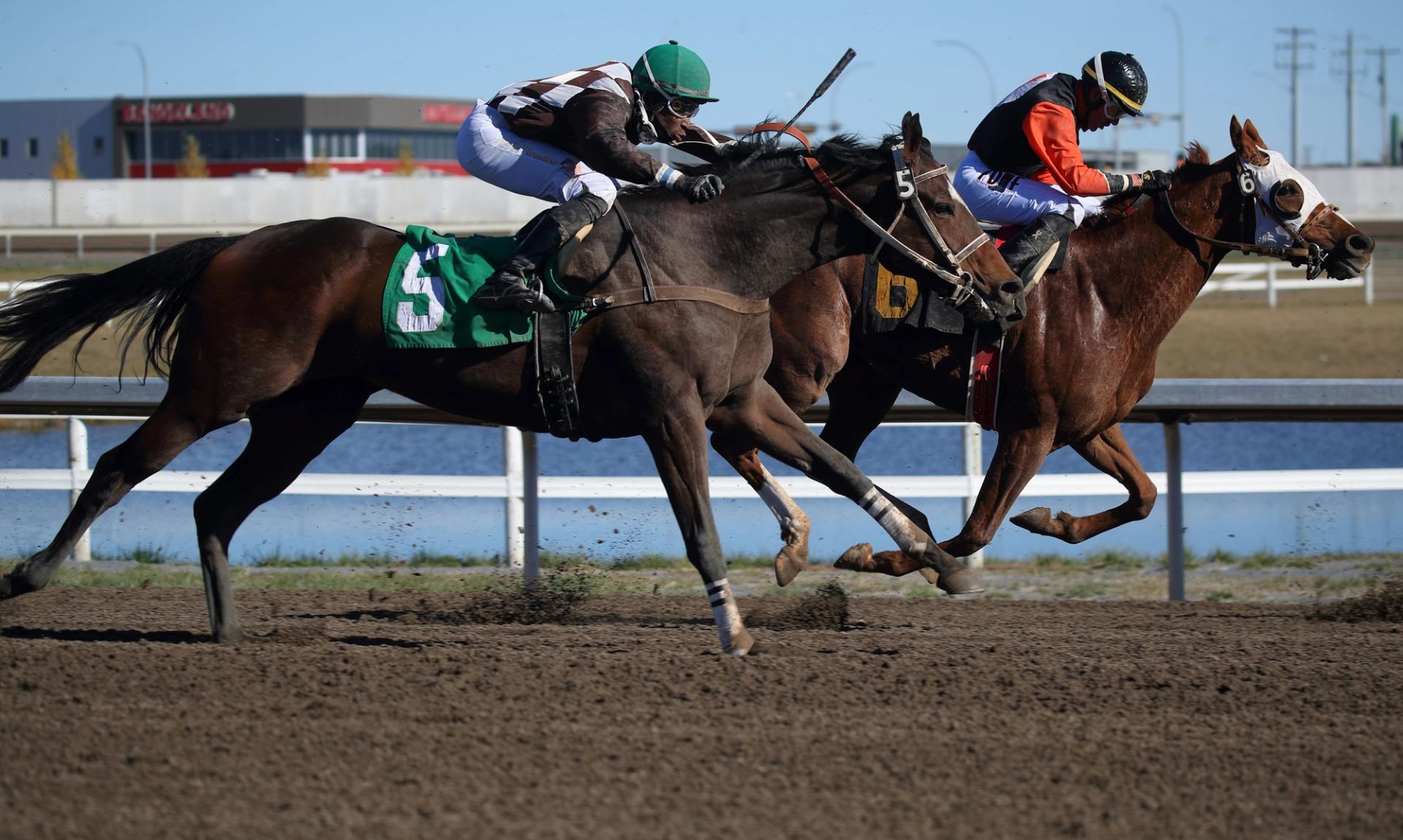 Two jockeys racing side by side on a dirt track.