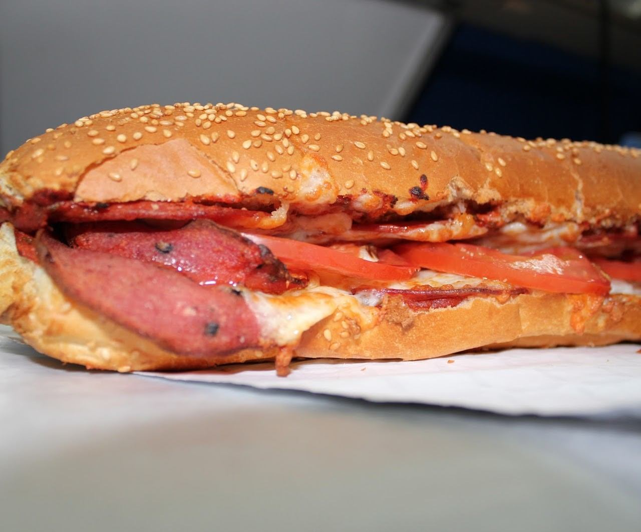 Close-up of a sesame hoagie filled with sliced meat, tomato, and melted cheese.