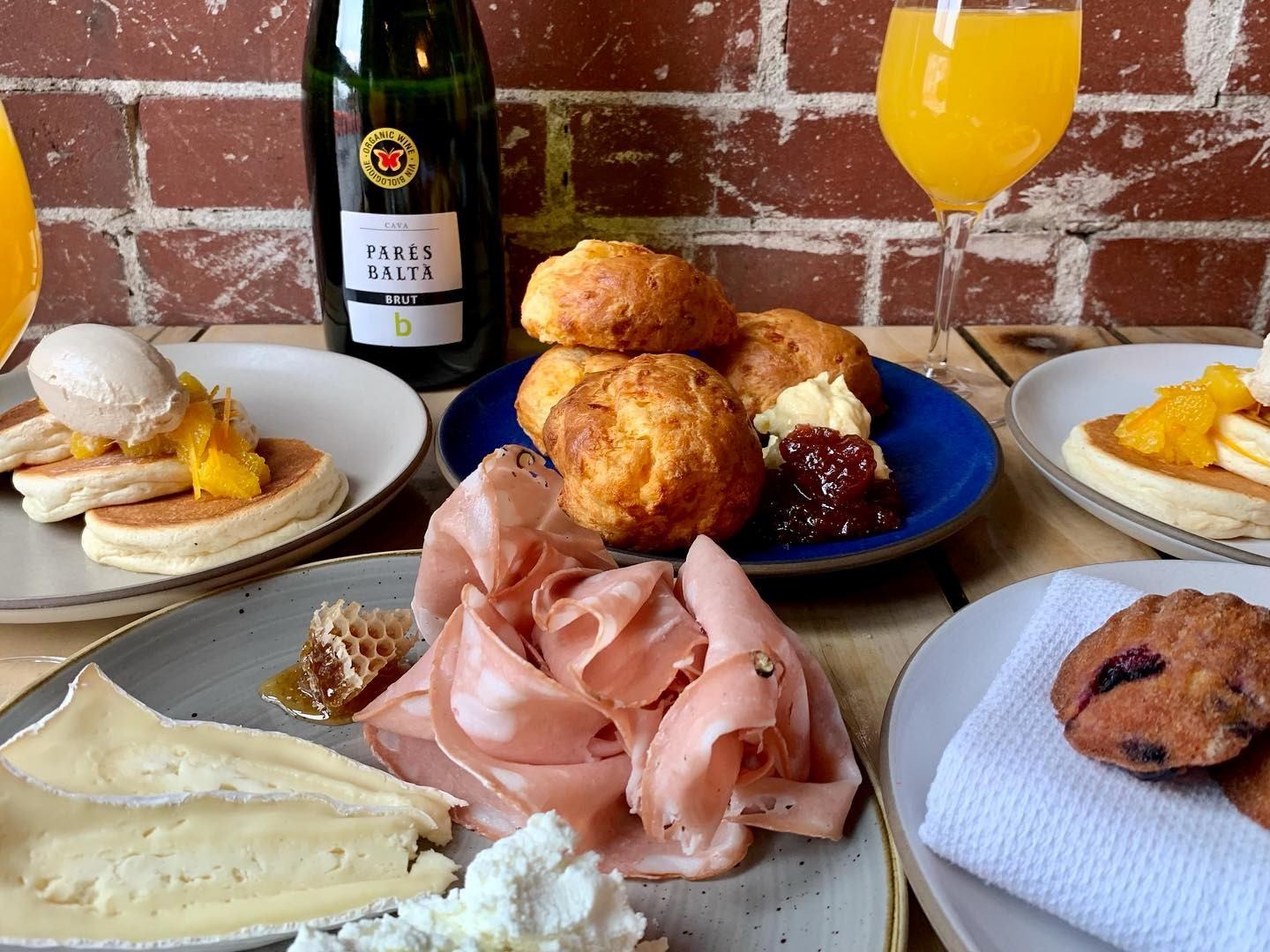Model Milk brunch spread with pastries, meats, cheeses, and mimosas by a brick wall.