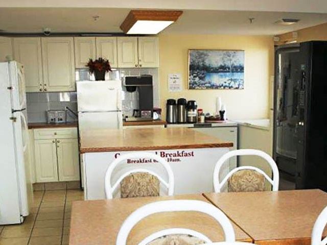 A clean continental breakfast station with white cabinets, coffee thermoses, and a toaster.