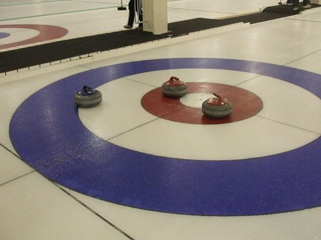 Curling stones resting in the house on an ice sheet.