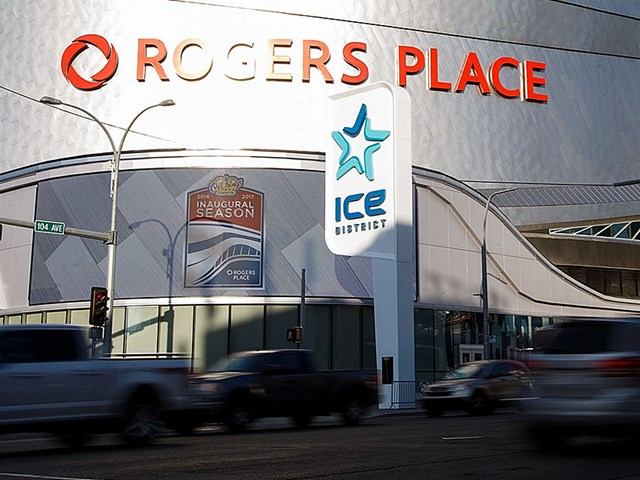 Rogers Place facade and ICE District sign beside street with passing cars.