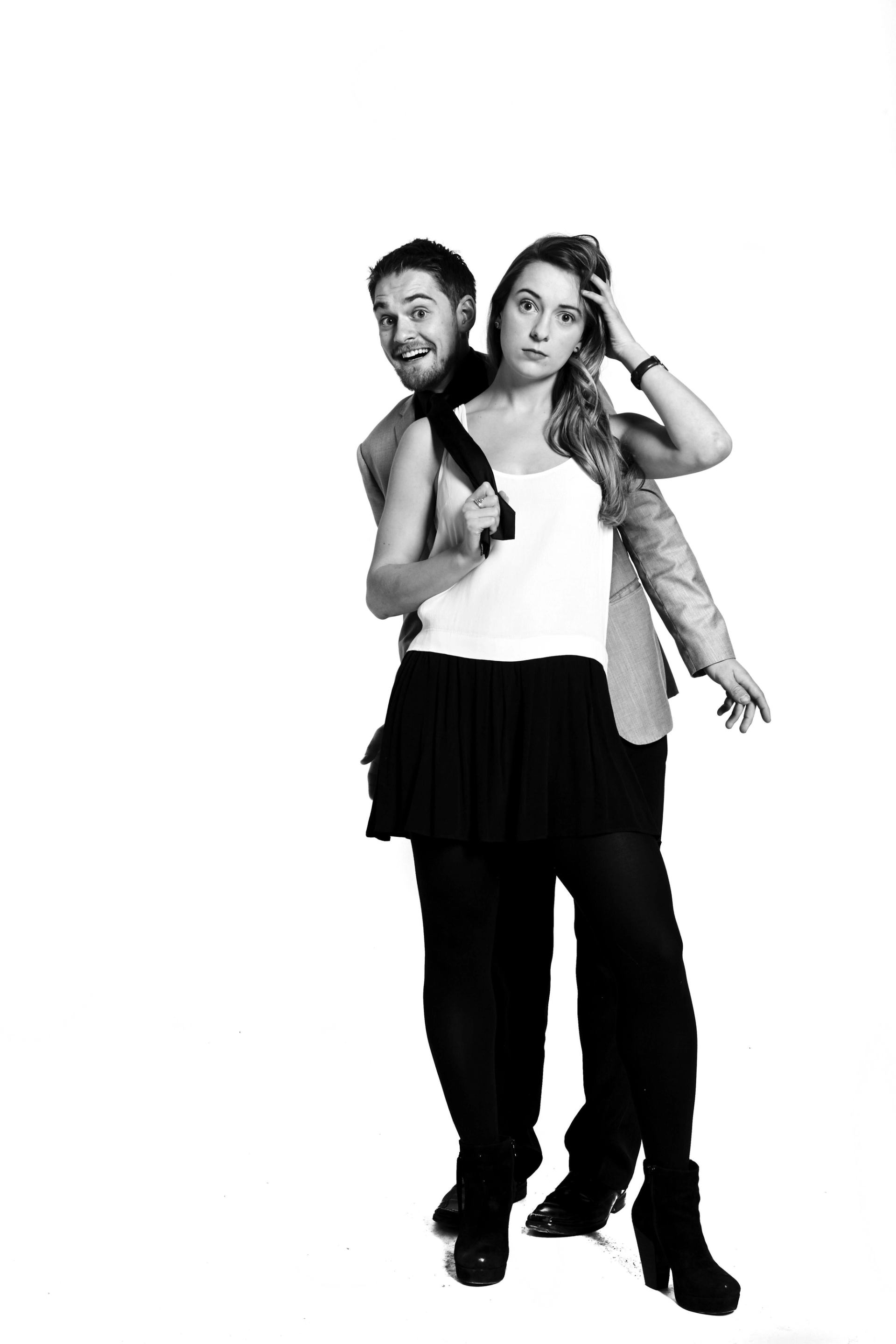 Two people pose in black-and-white studio portrait, one holding a necktie.