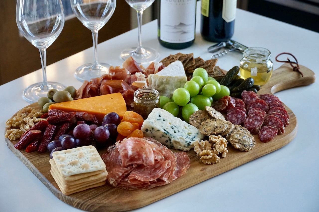 Charcuterie board with cheeses, meats, fruits, nuts, and wine glasses.