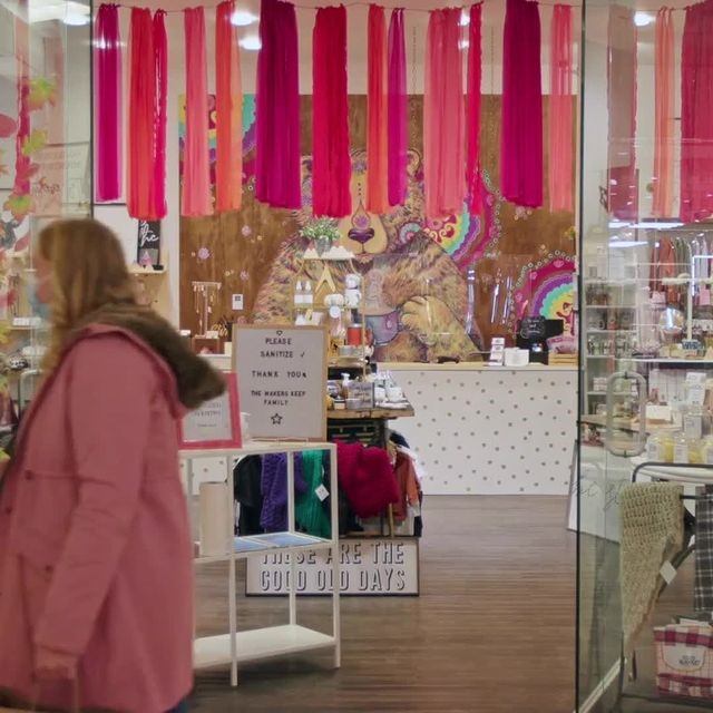 Mall storefront with display counter, colorful curtains, and people walking past.