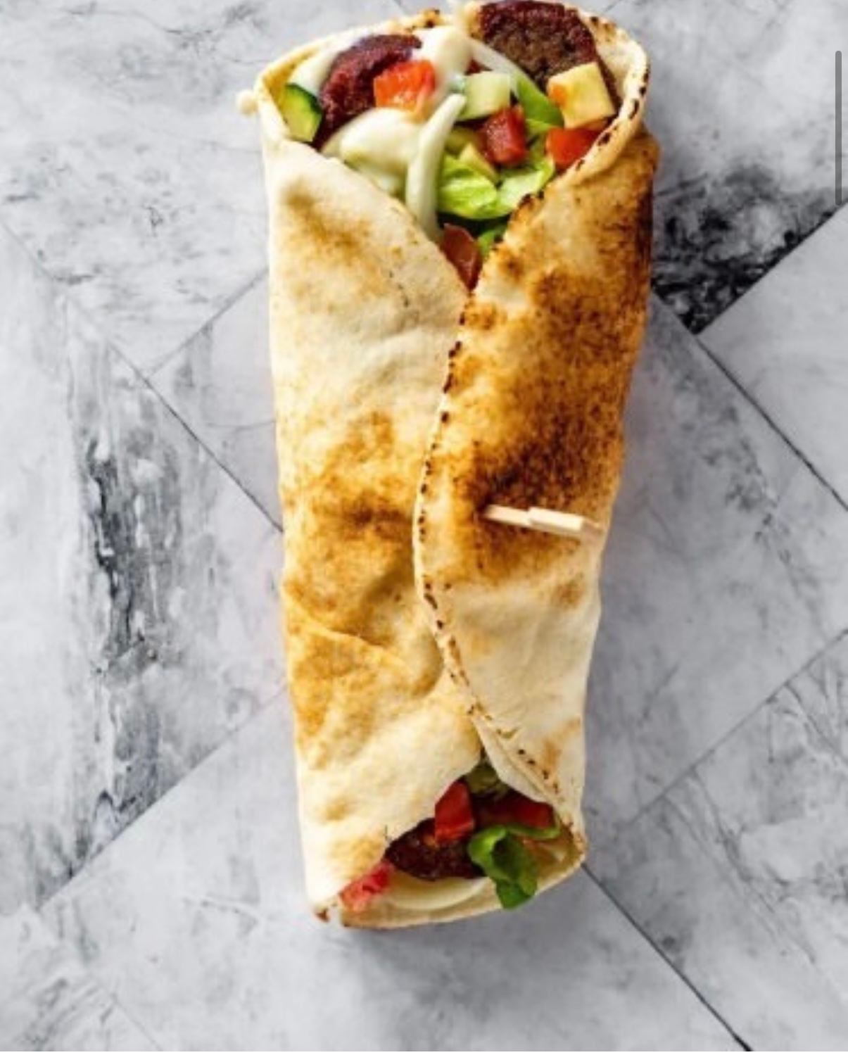 Fresh wrap with lettuce, tomato, cucumber, and grilled meat on a marble surface.
