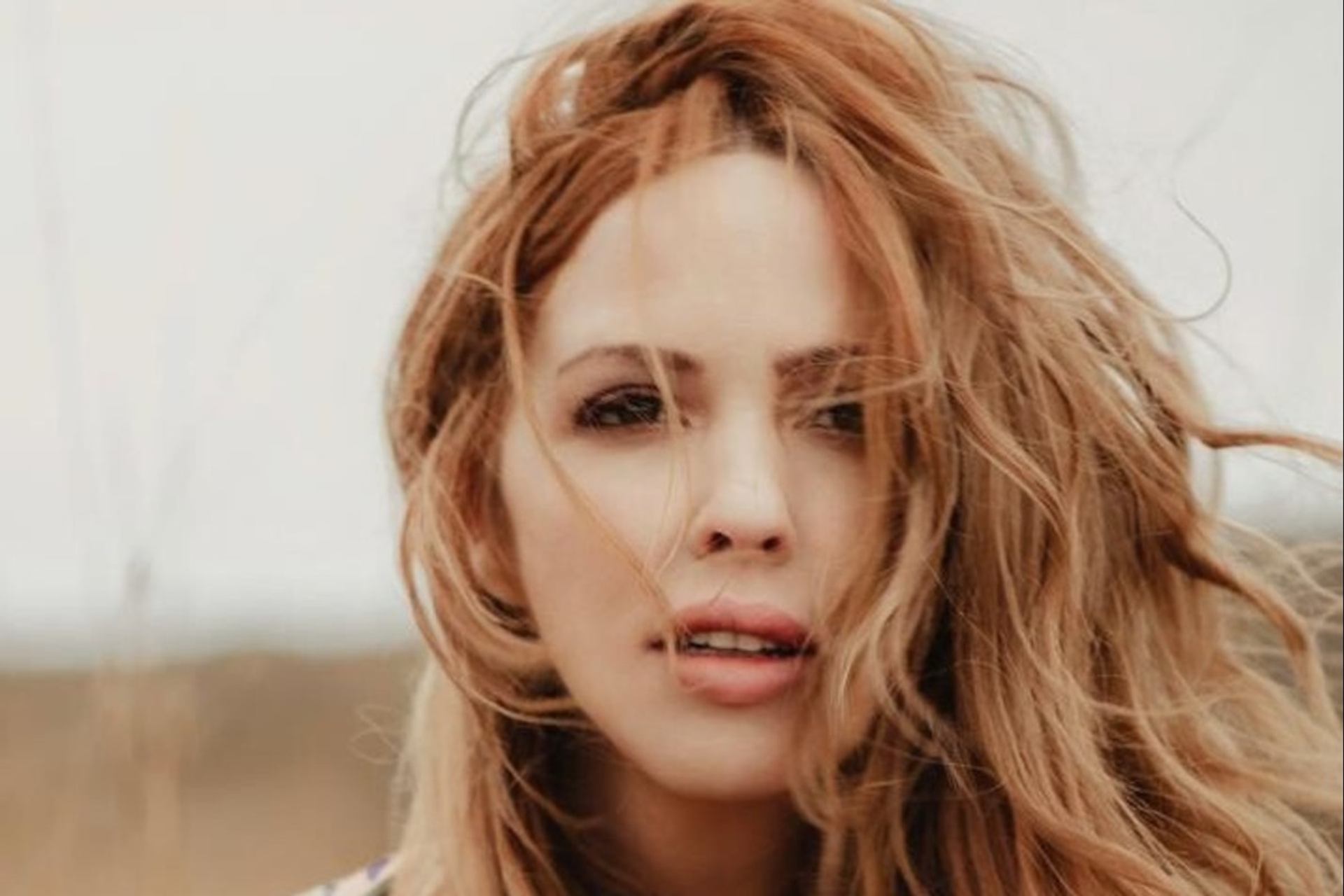 A woman with wind-blown auburn hair looking directly at the camera.