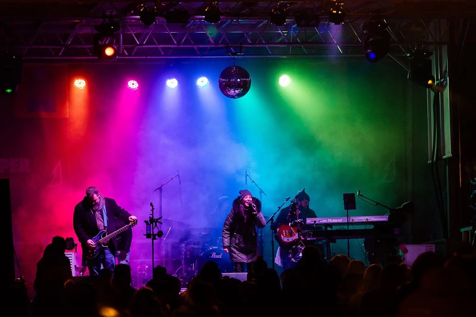 Live band performing on stage under colorful lights and smoke effects.
