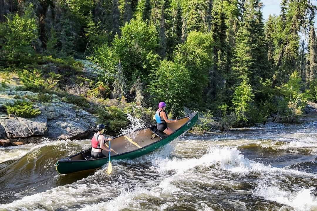Canoeists ride whitewater rapids through forested terrain at HeLa Ventures.