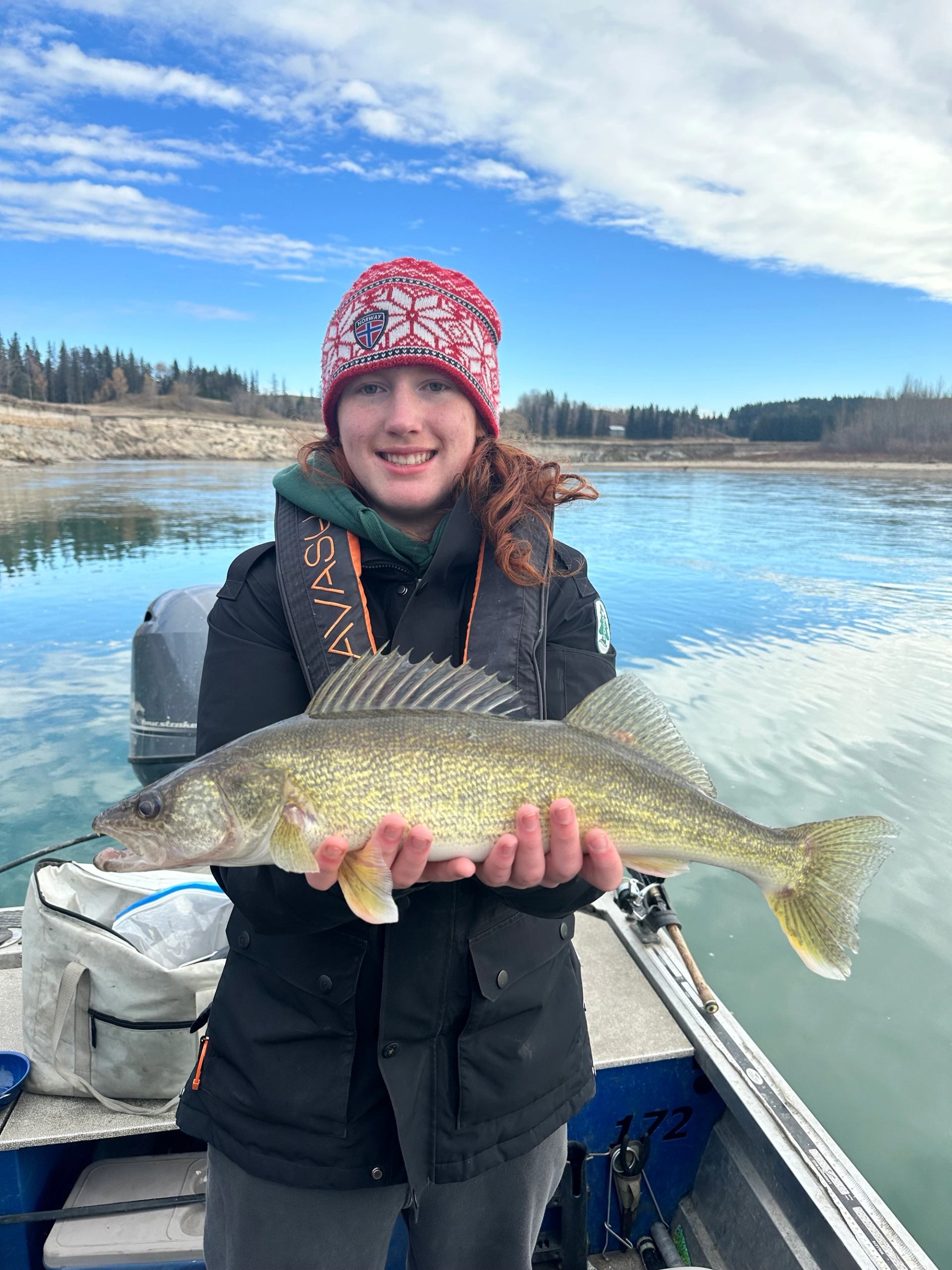 Person in red knit hat holding a large fish on a boat on a frozen lake.