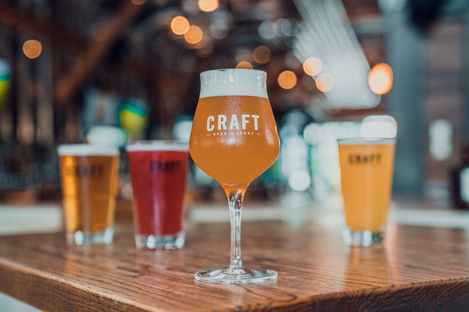 Four colorful craft beers on a wooden table in a cozy bar setting.