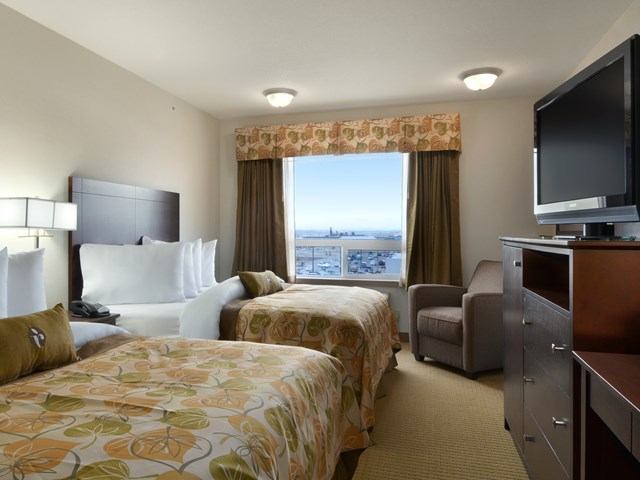 Hotel room with two single beds, TV, armchair, and city view window.