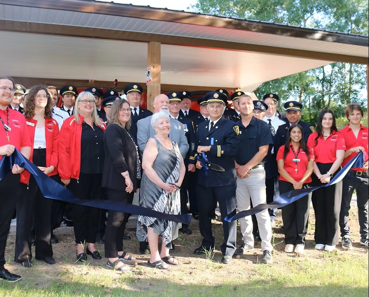 Uniformed officers and community members pose behind a blue ribbon outdoors.