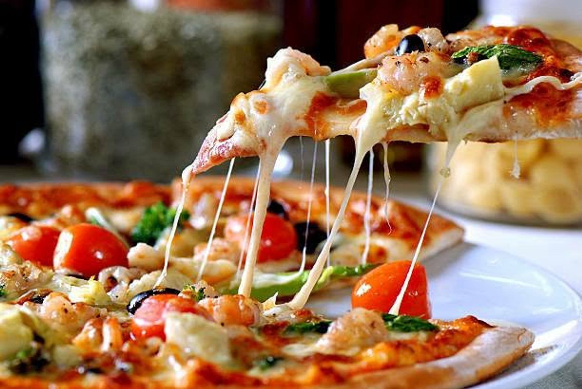 Pizza slice lifted from a vegetable and shrimp pizza with melted cheese stretching.