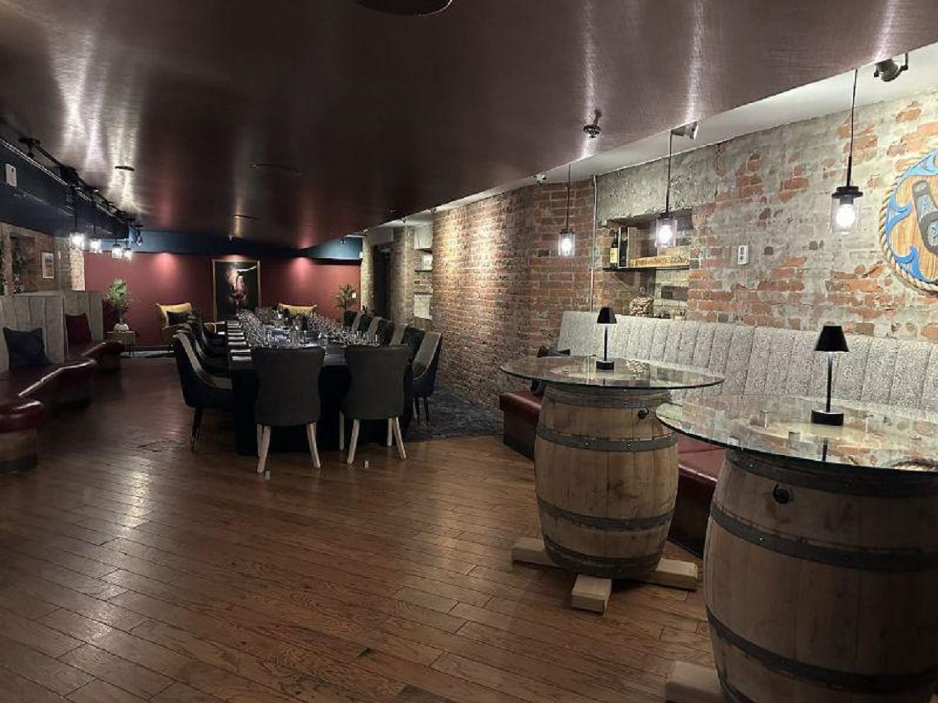 Underground dining room with exposed brick walls, barrel tables, and warm ambient lighting at CavernUs.