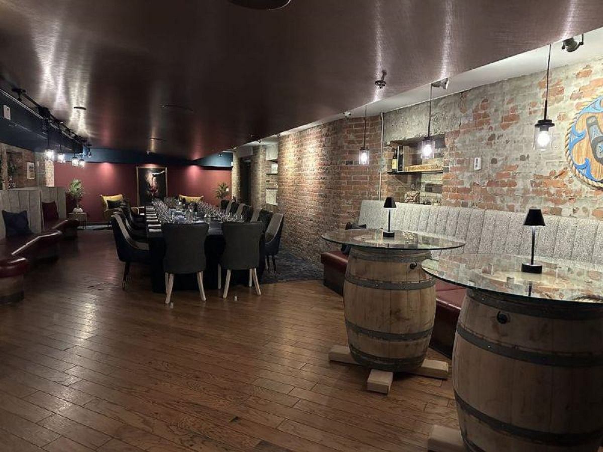 Underground dining room with exposed brick walls, barrel tables, and warm ambient lighting at CavernUs.
