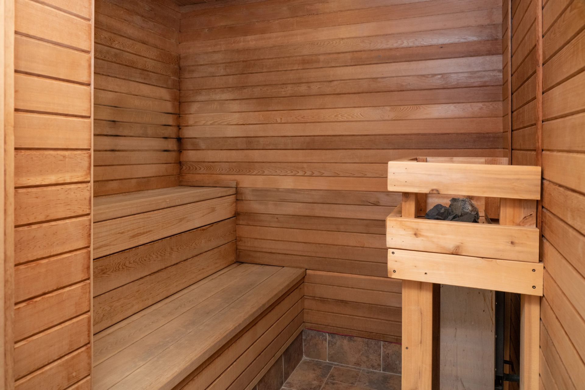 Wooden sauna interior with tiered benches and stone-tiled floor.