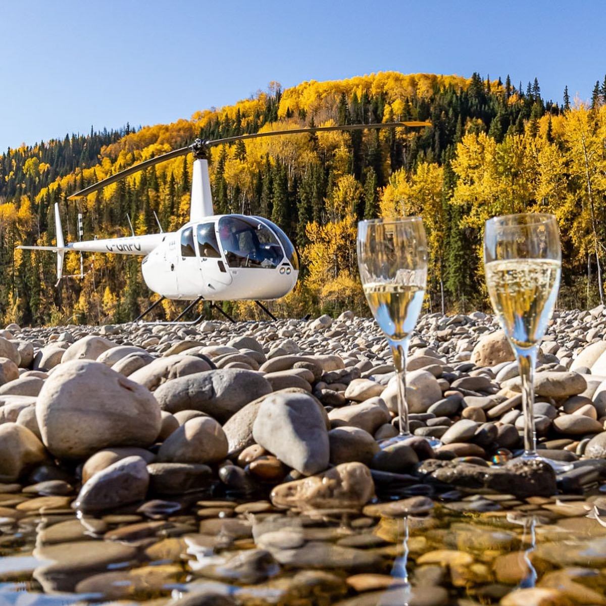 Helicopter above autumn forest with champagne glasses on rocky riverbed.