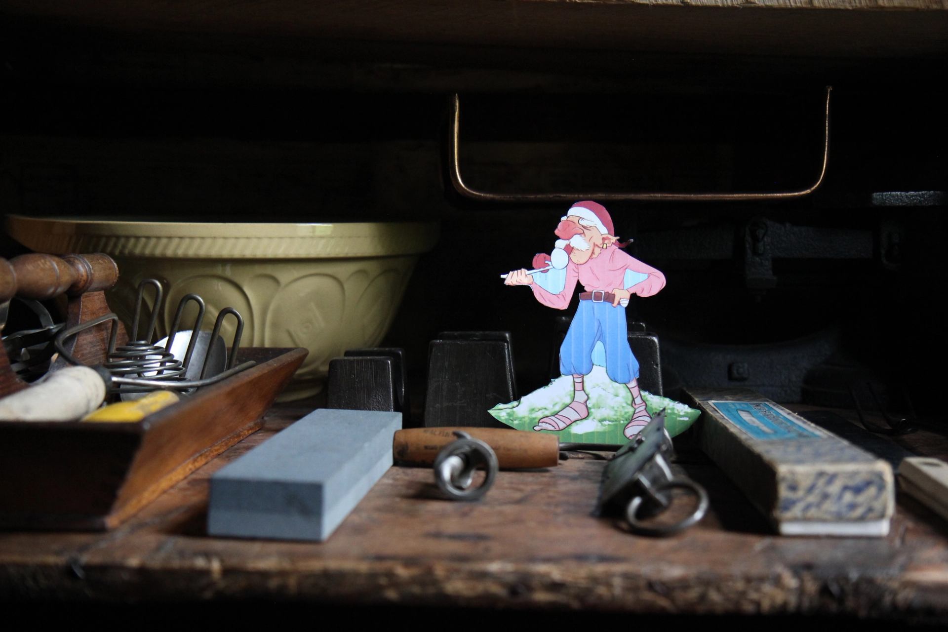 Wooden workbench with vintage tools and cartoon cut-out figure in front of bowl.