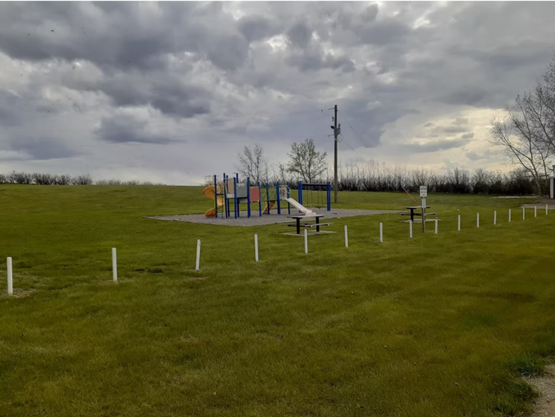 Playground with slides and swings in open grassy field under cloudy sky.